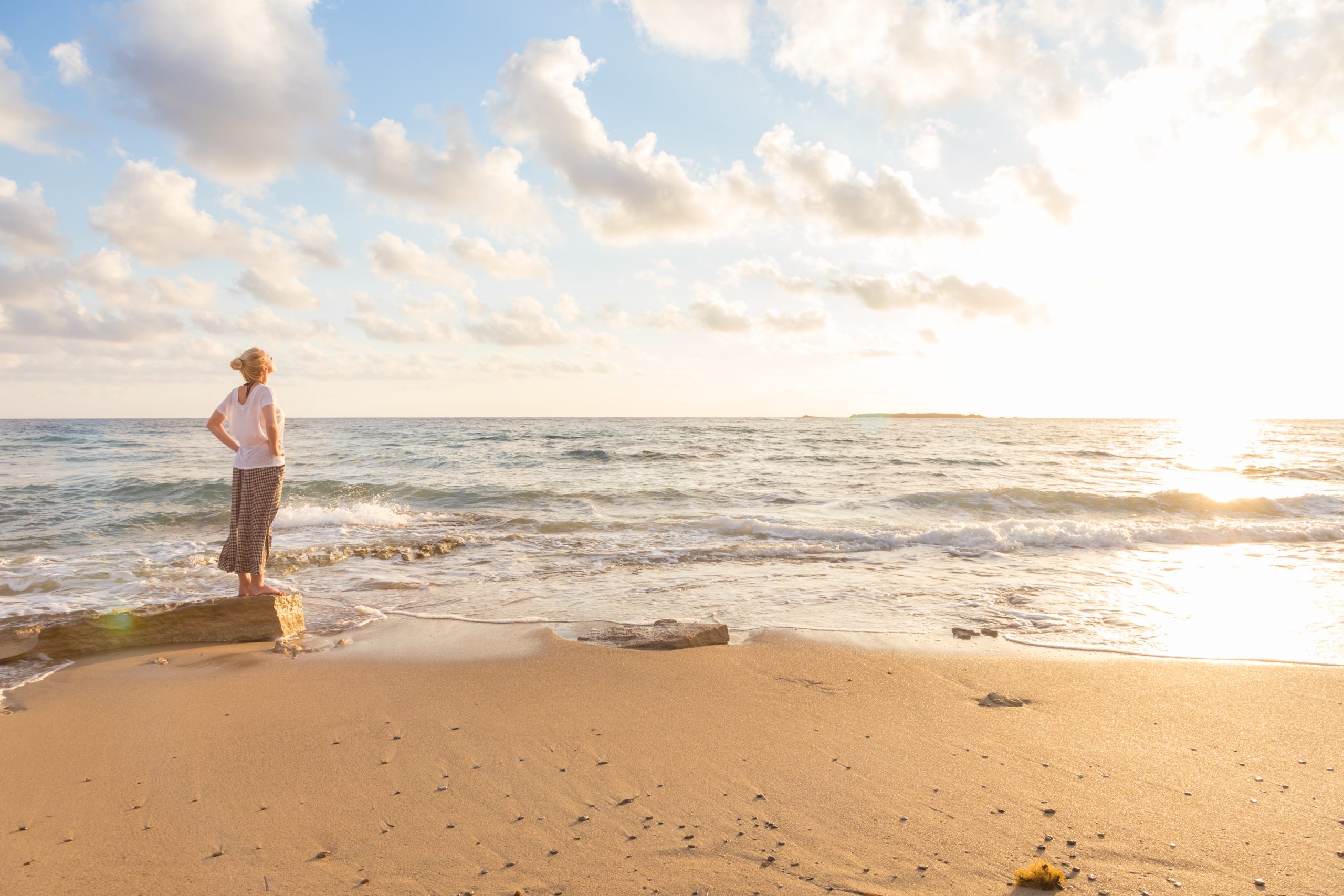 Relaxed woman enjoying sun, freedom and life an beautiful beach in sunset. Young lady feeling free, relaxed and happy. Concept of vacations, freedom, happiness, enjoyment and well being.